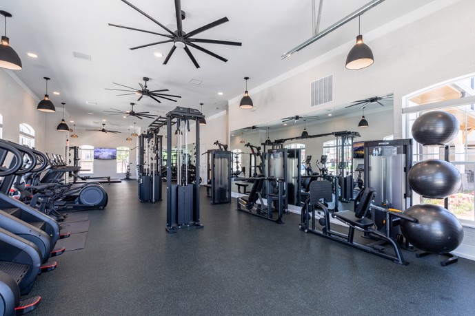 Spacious indoor fitness center with ceiling fans, equipped with a variety of exercise machines along the walls and down the center